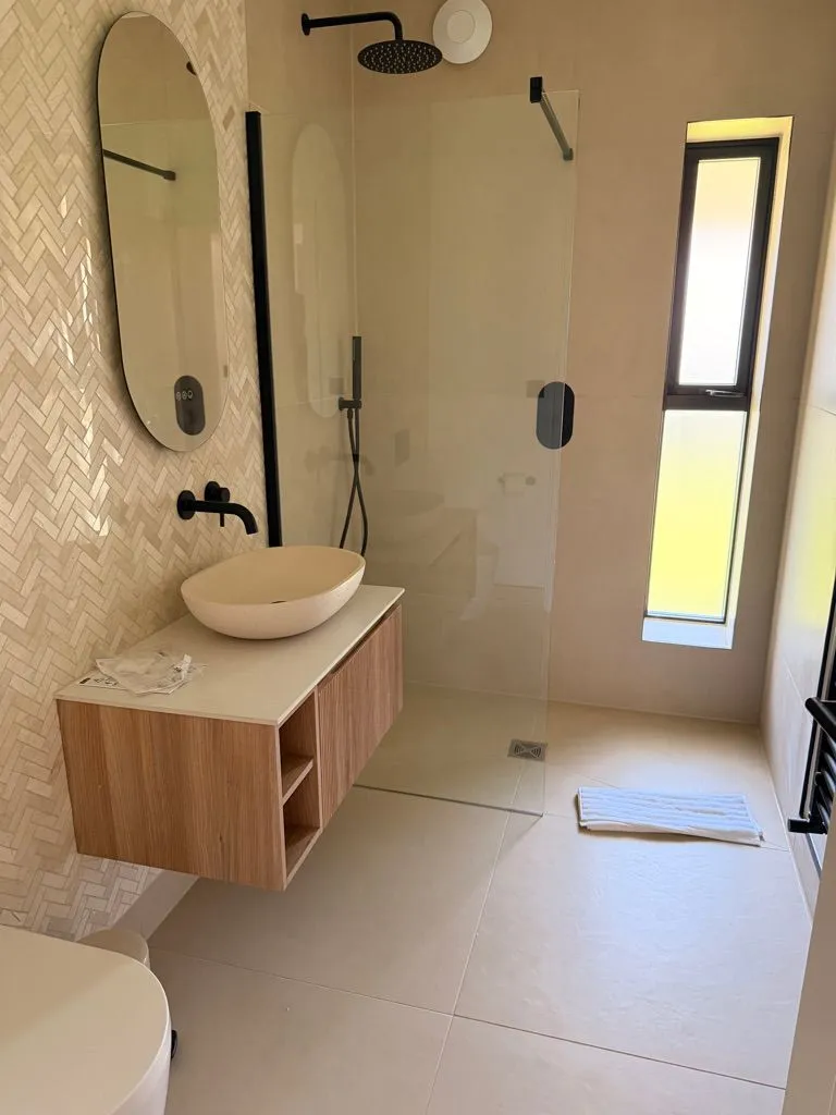 Completed bathroom with herringbone tiled walls, wall-hung vanity and glass shower screen