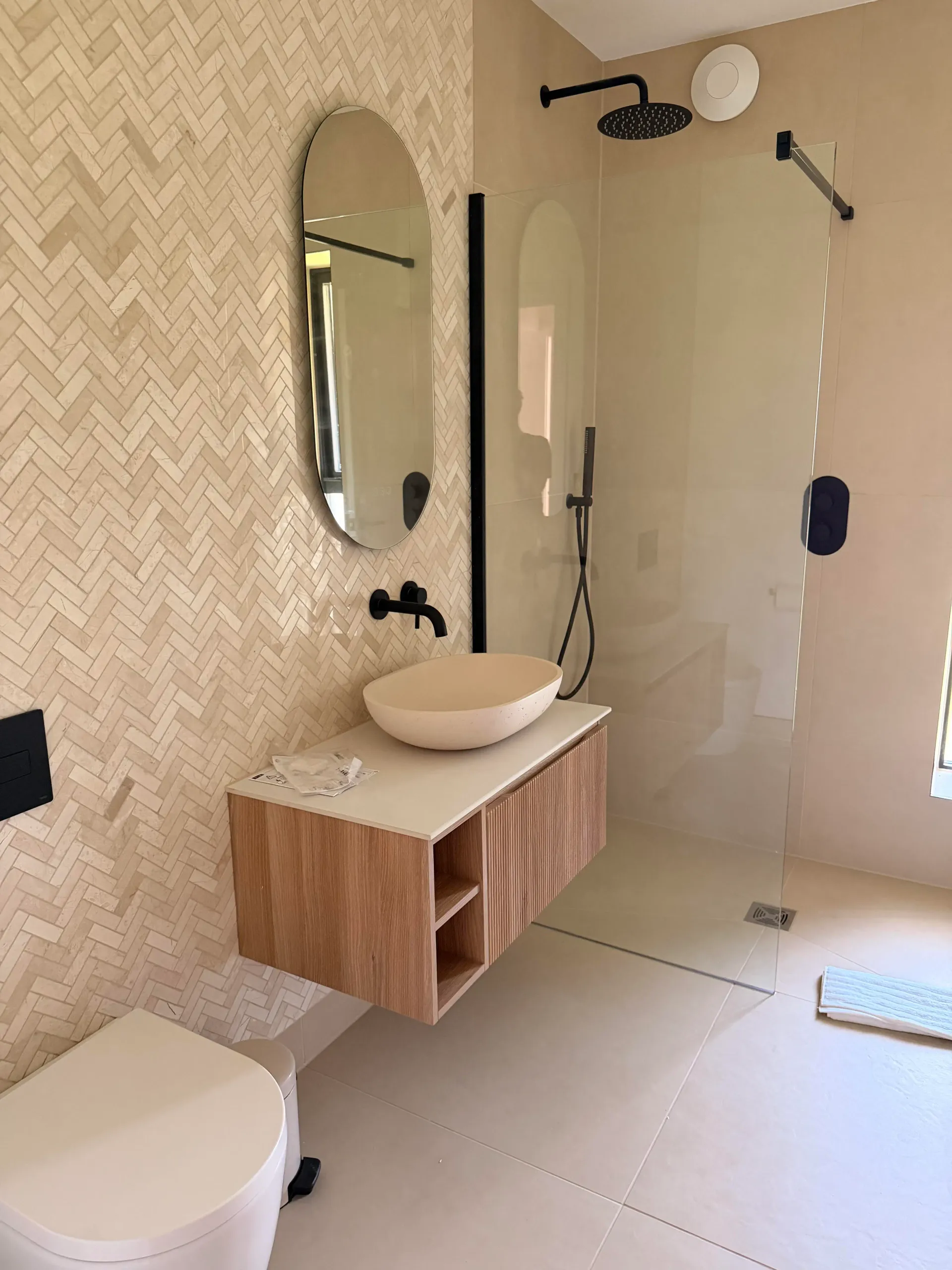 Completed bathroom with herringbone tiling, wall-hung vanity and glass shower screen