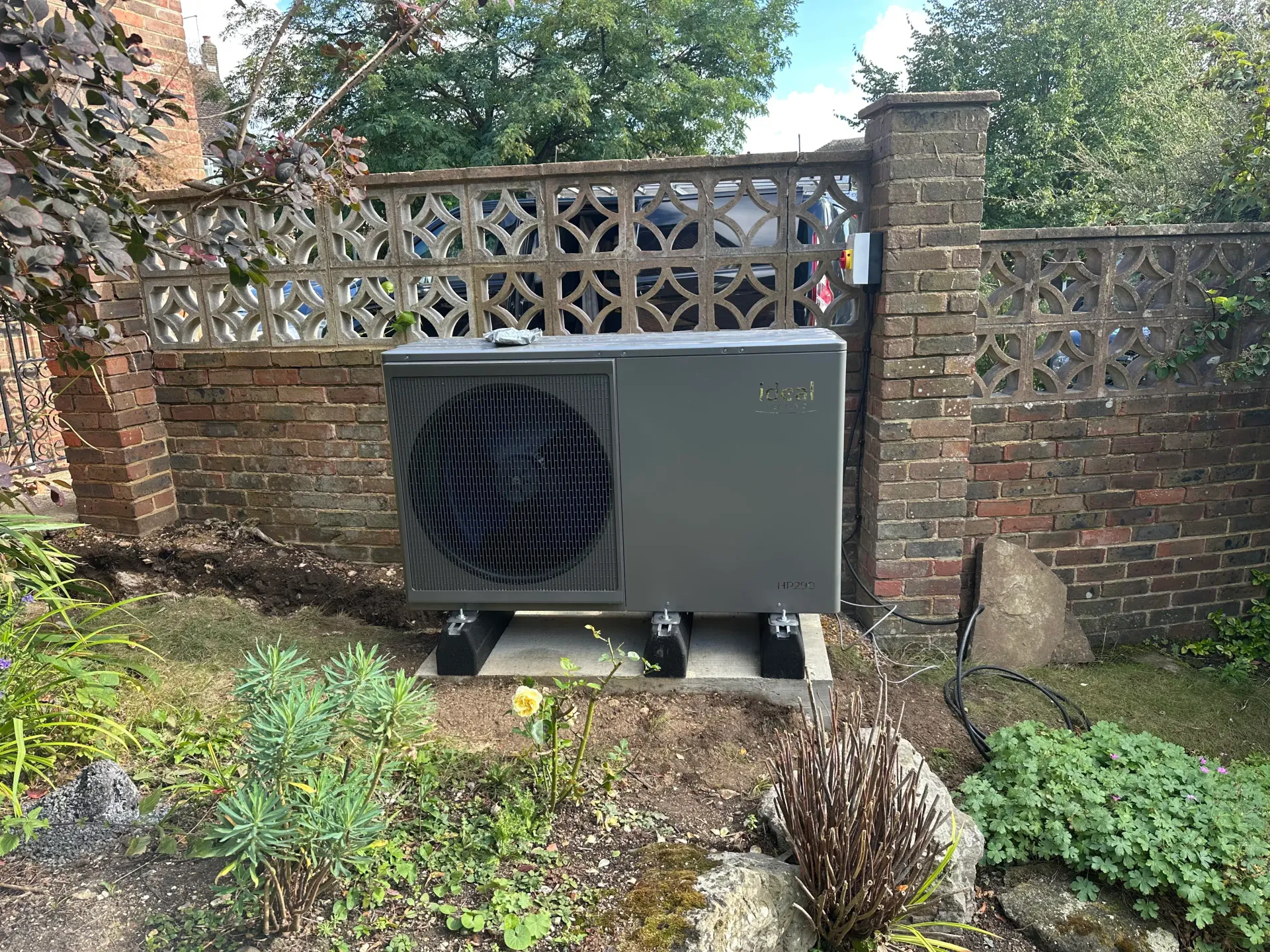 External air source heat pump unit installed on a concrete plinth in a garden