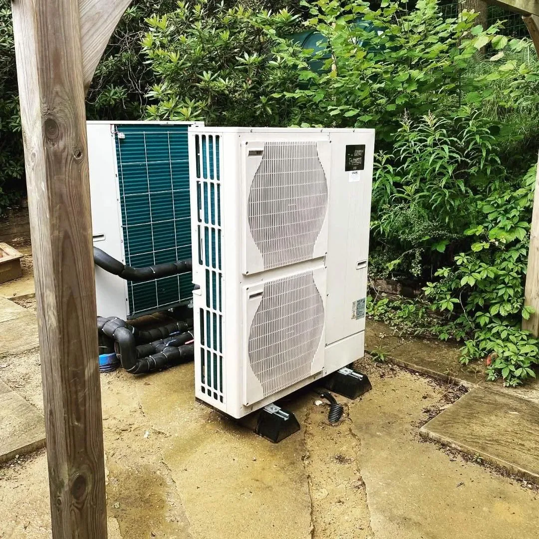 Outdoor HVAC condenser unit installed on a concrete pad beside a garden