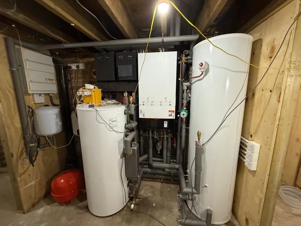 Twin hot water cylinders and boiler with manifold pipework in a timber-framed plant room